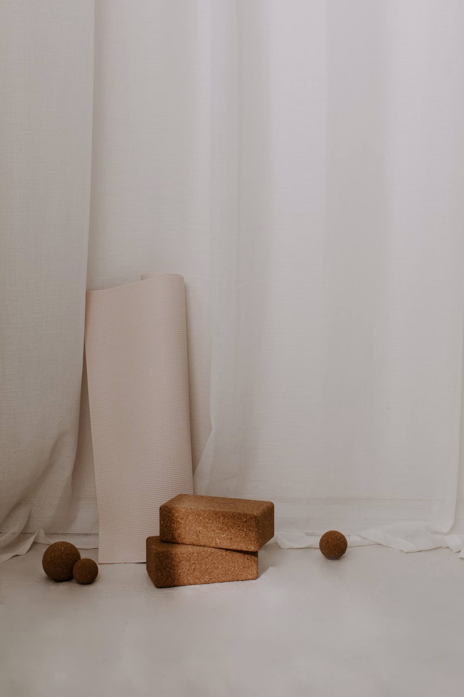 Rolled yoga mat and cork blocks against white linen curtains