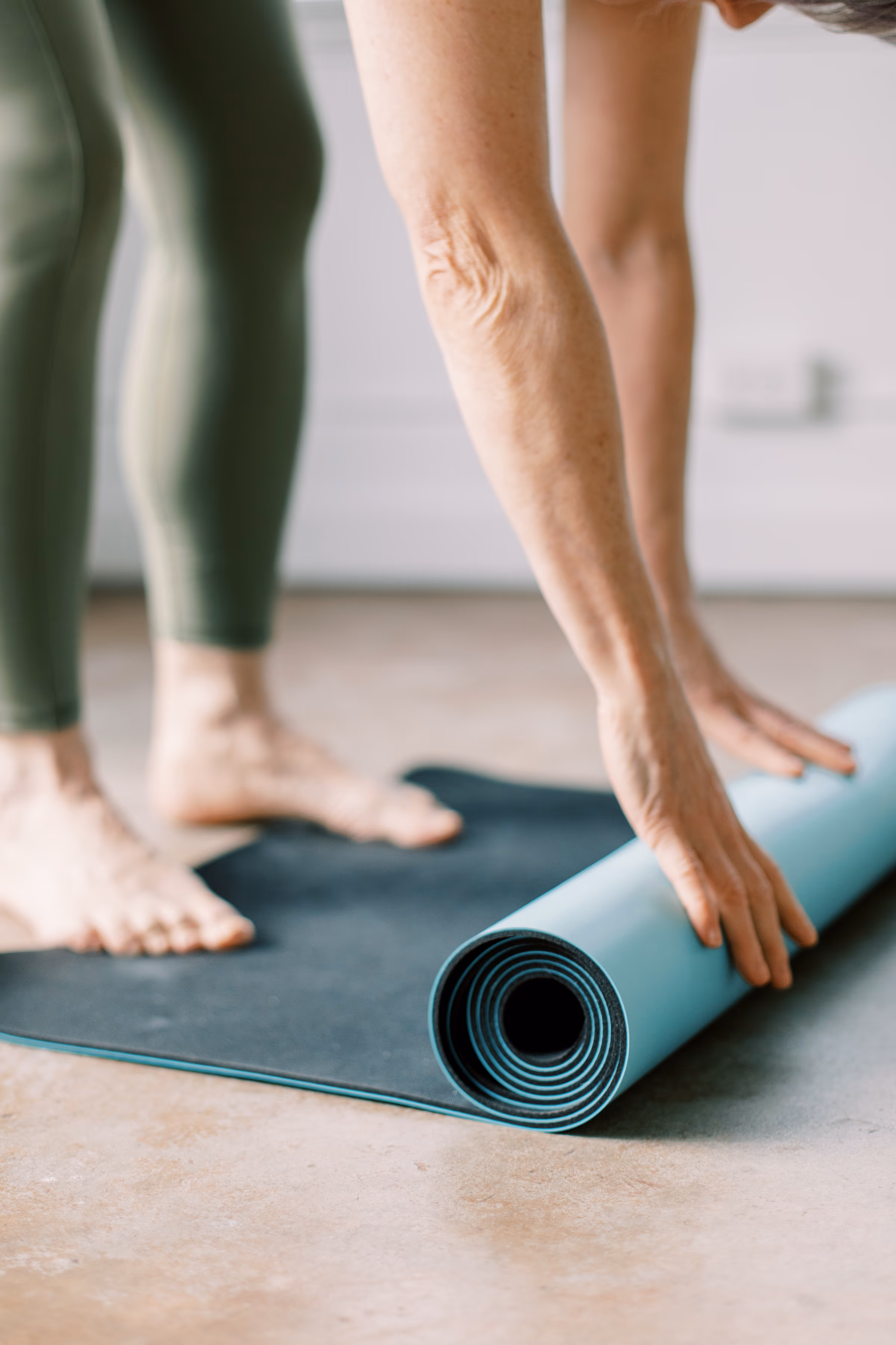 Woman unrolling a yoga mat, bare feet on a studio floor