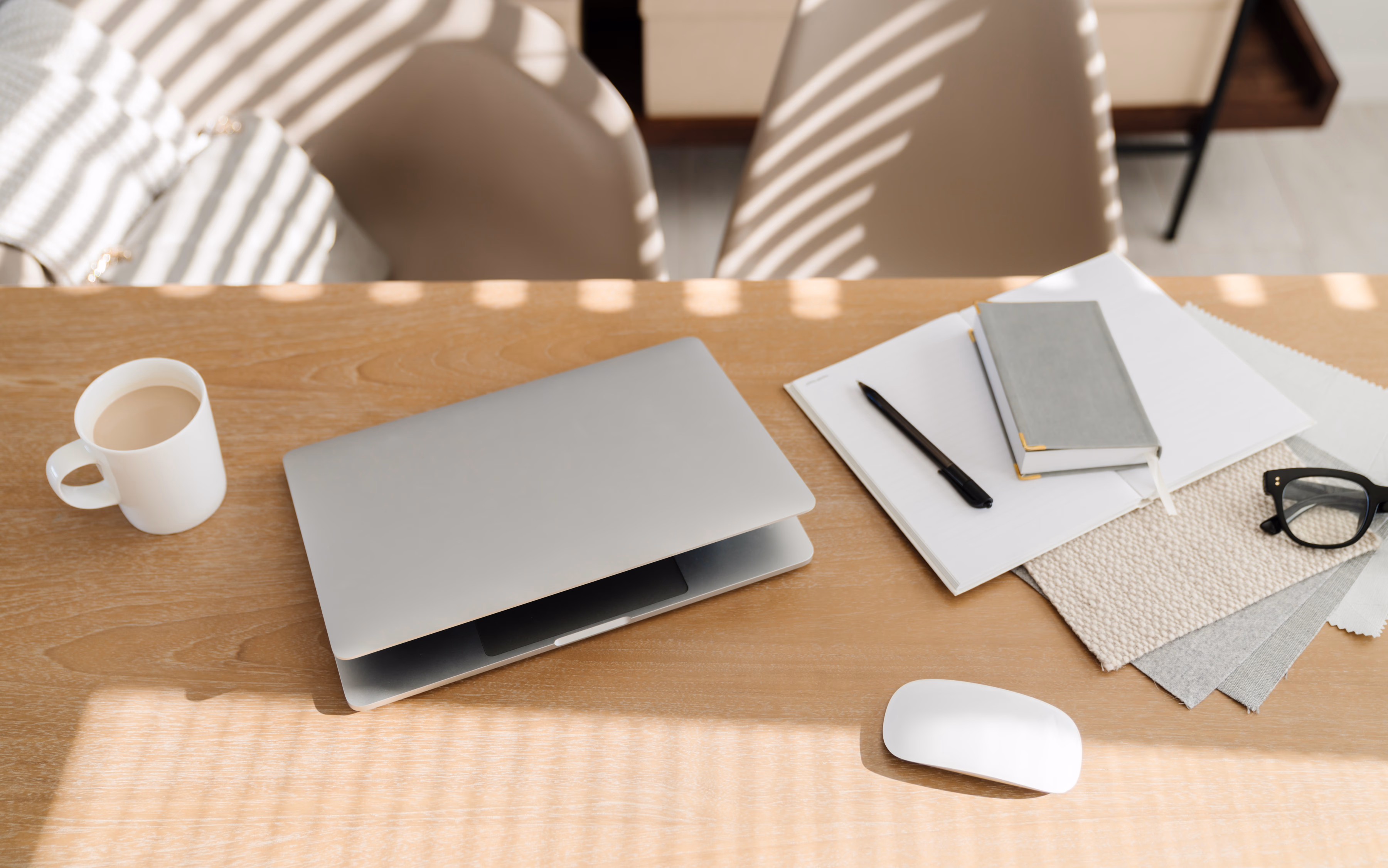 Desk flatlay with laptop, notebook, coffee and glasses in warm morning light