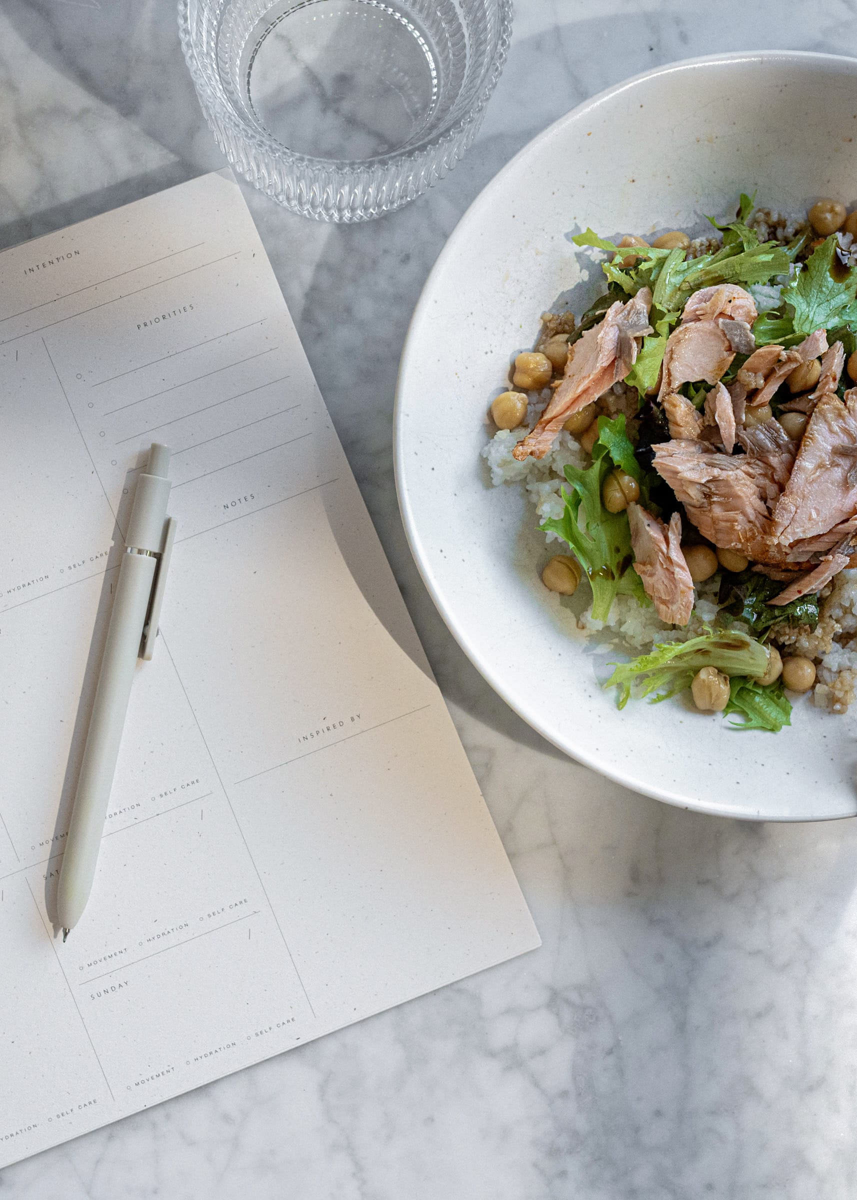 Salmon and chickpea bowl beside a planning notepad on marble