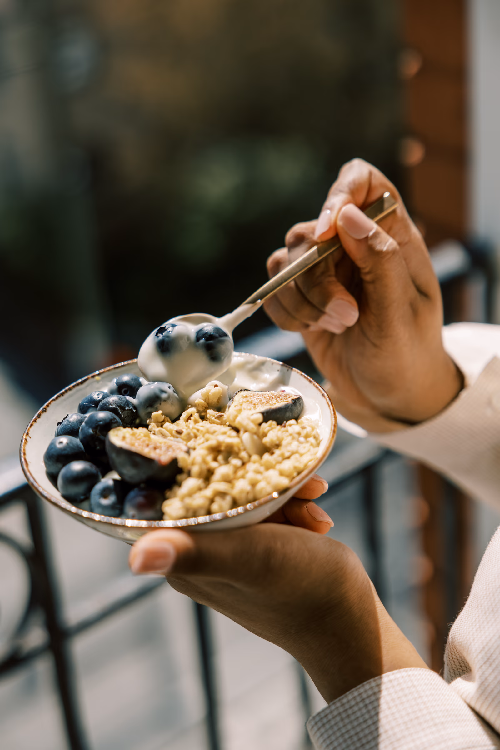 Hands holding a bowl of granola with blueberries and yogurt