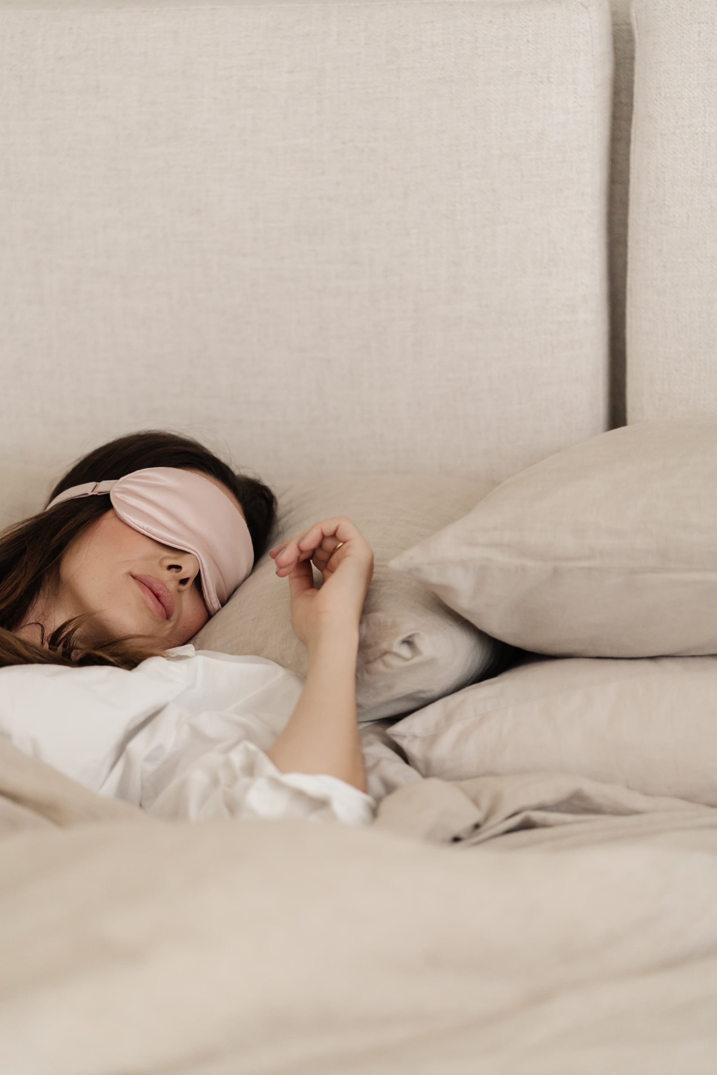 Woman sleeping with a pink silk eye mask in soft linen bedding