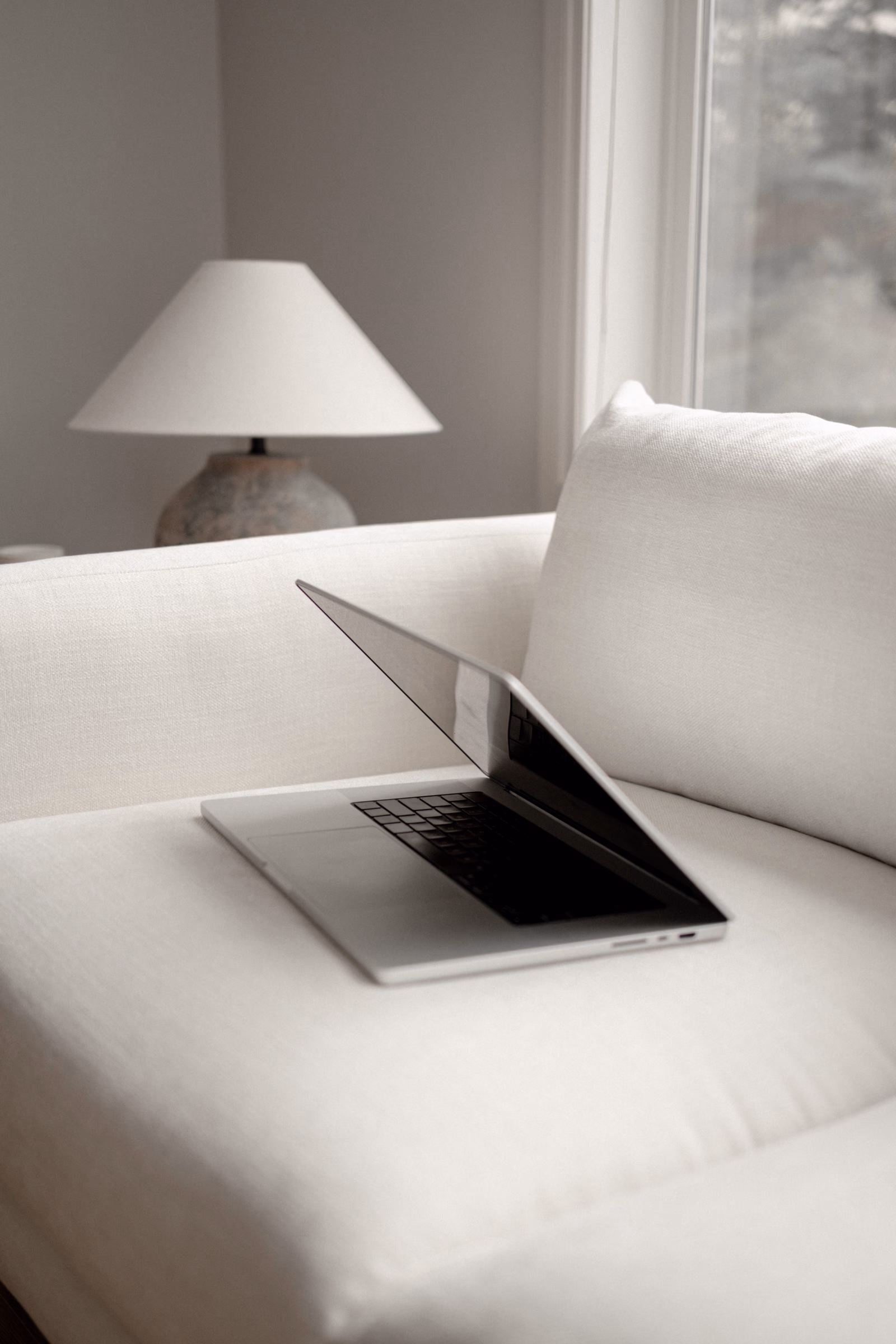 Open laptop on a white sofa with a lamp in a calm home setting