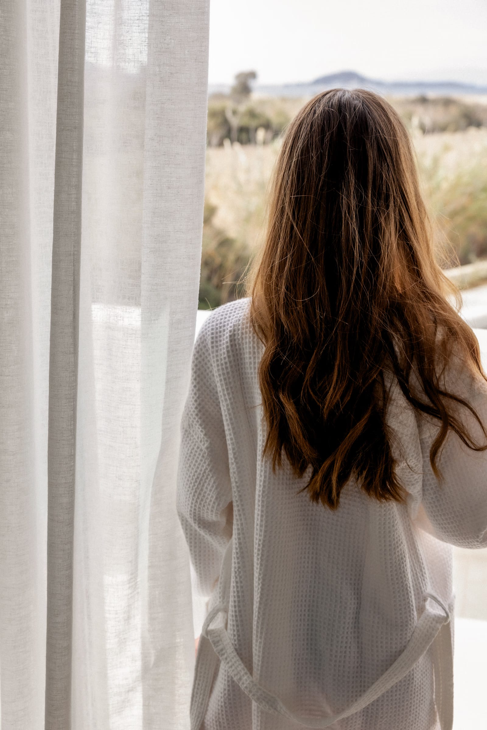 Woman in a robe looking out at a landscape, in a quiet morning moment